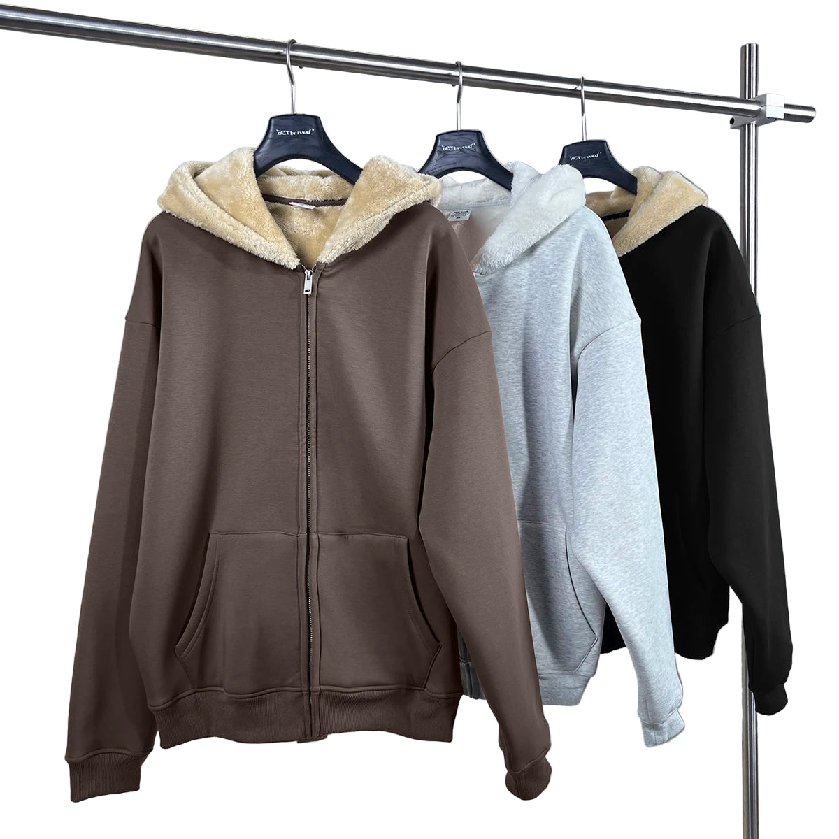 Three hoodies in brown, gray, and black hanging on a rack with a white background.