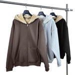 Three hoodies in brown, gray, and black hanging on a rack with a white background.