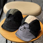 Two hats, one black and green, the other gray and black, on a round wooden table.
