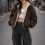 Woman wearing a brown jacket, white top, and black pants on an urban street.