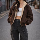 Woman wearing a brown jacket, white top, and black pants on an urban street.