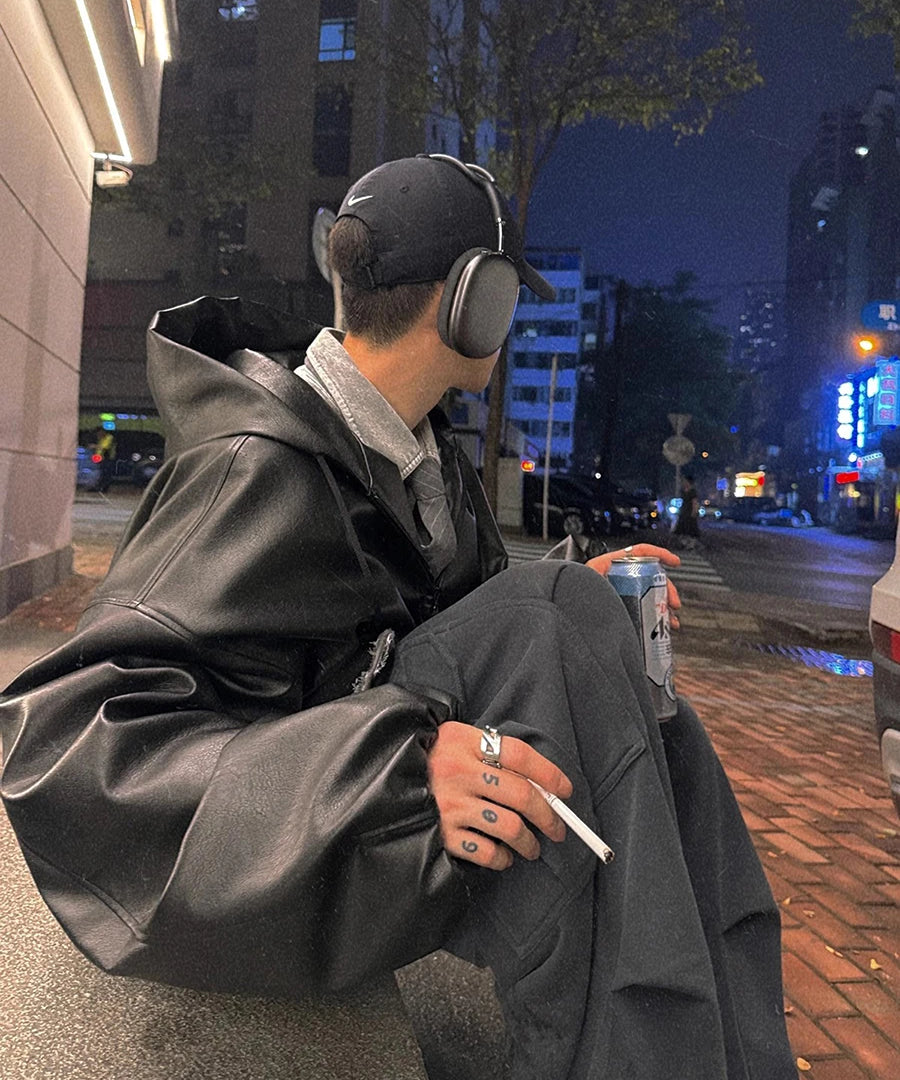 Person sitting on a street corner at night, wearing headphones and holding a cigarette.