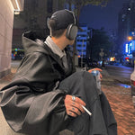 Person sitting on a street corner at night, wearing headphones and holding a cigarette.