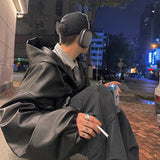 Person sitting on a street corner at night, wearing headphones and holding a cigarette.