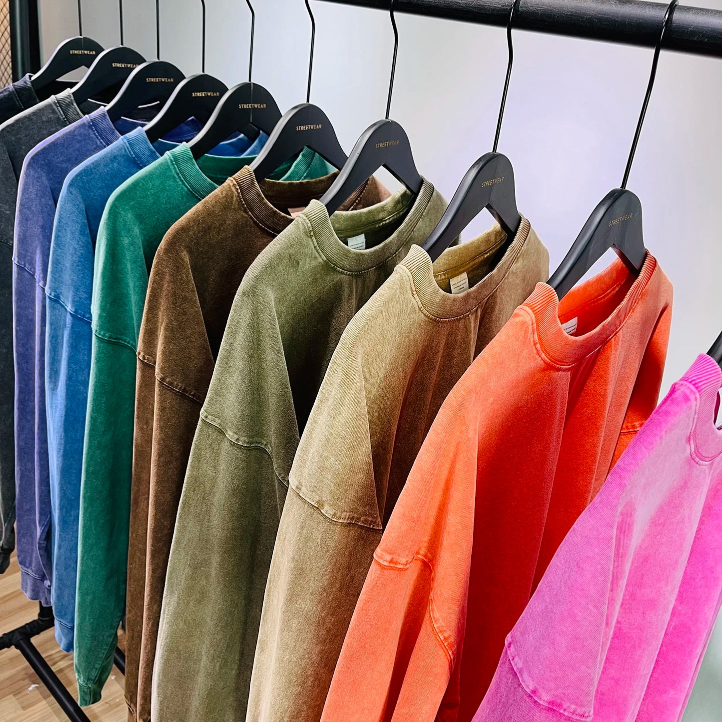 Row of colorful sweatshirts on hangers against a neutral background