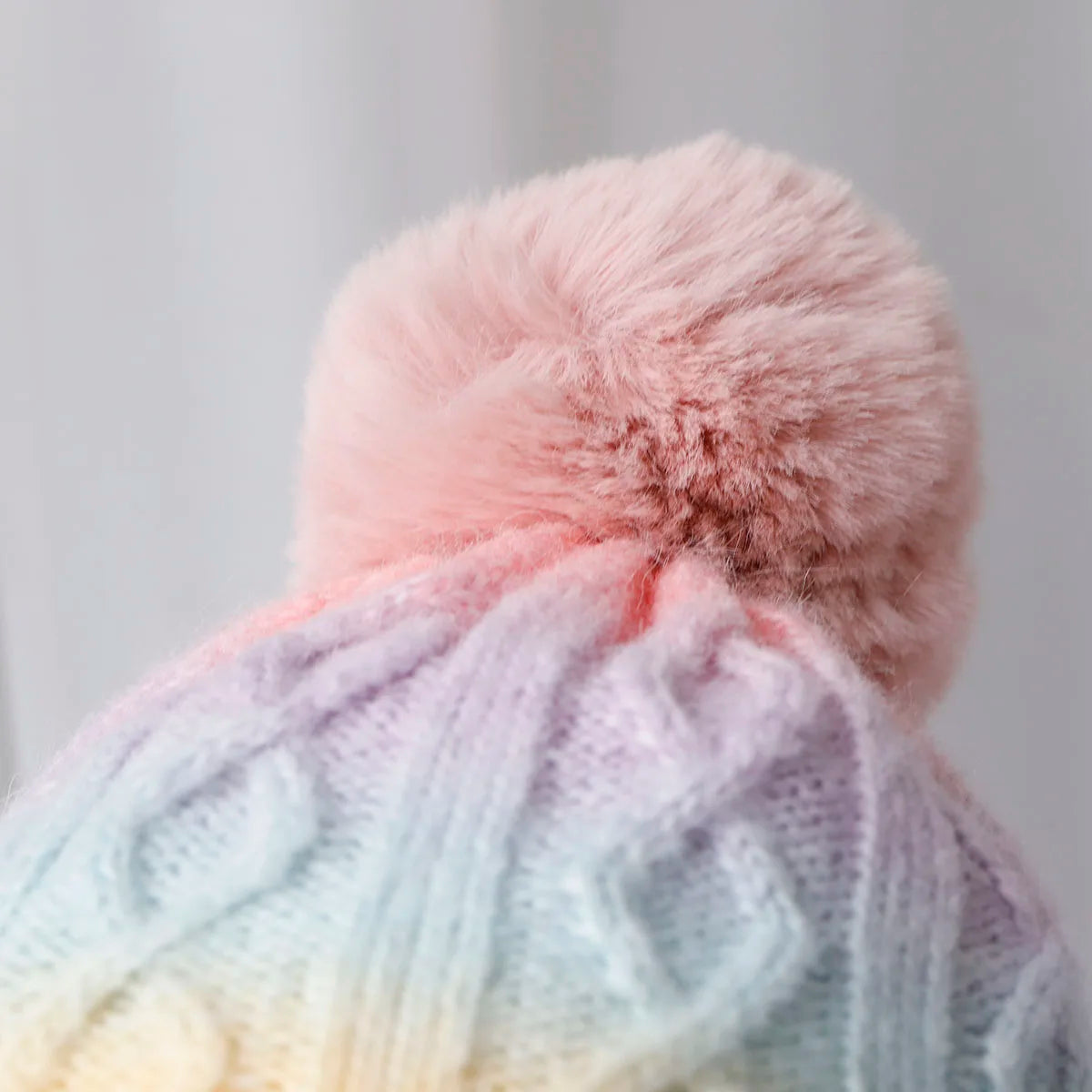 Pastel-colored knit hat with a fluffy pink pom-pom on a light gray background