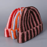 Three striped knit hats in red, orange, and brown on a gray background