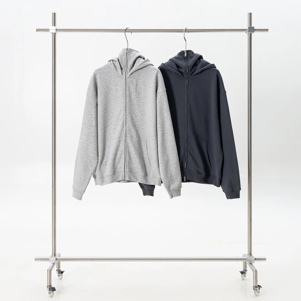 Two hoodies, one gray and one black, hanging on a metal clothing rack against a white background.