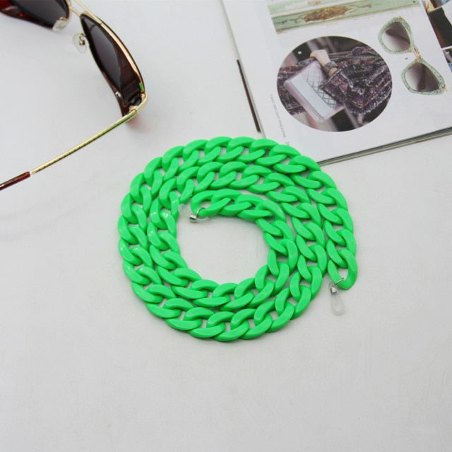 Neon Green Glasses chain coiled flat lay beside sunglasses and open magazine