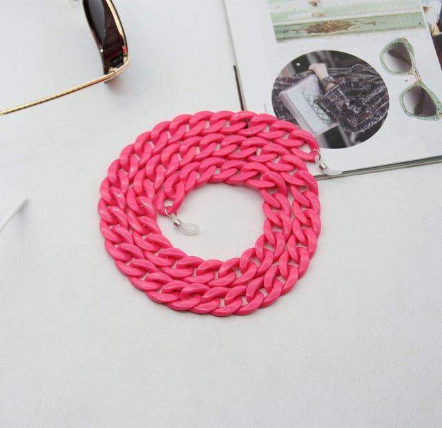 Neon Pink Glasses chain coiled flat lay next to sunglasses and magazine