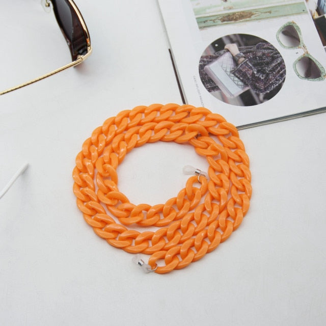 Orange Glasses chain coiled flat lay beside sunglasses and open magazine